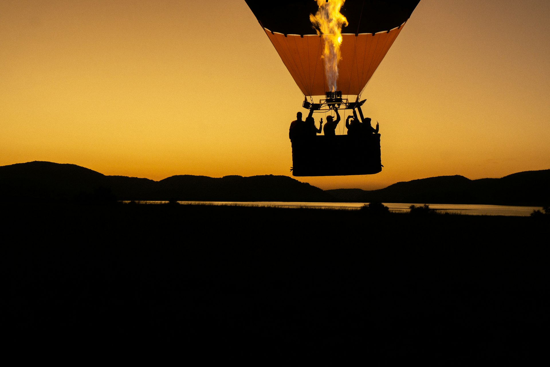 A hot air balloon flying over a lake at sunset